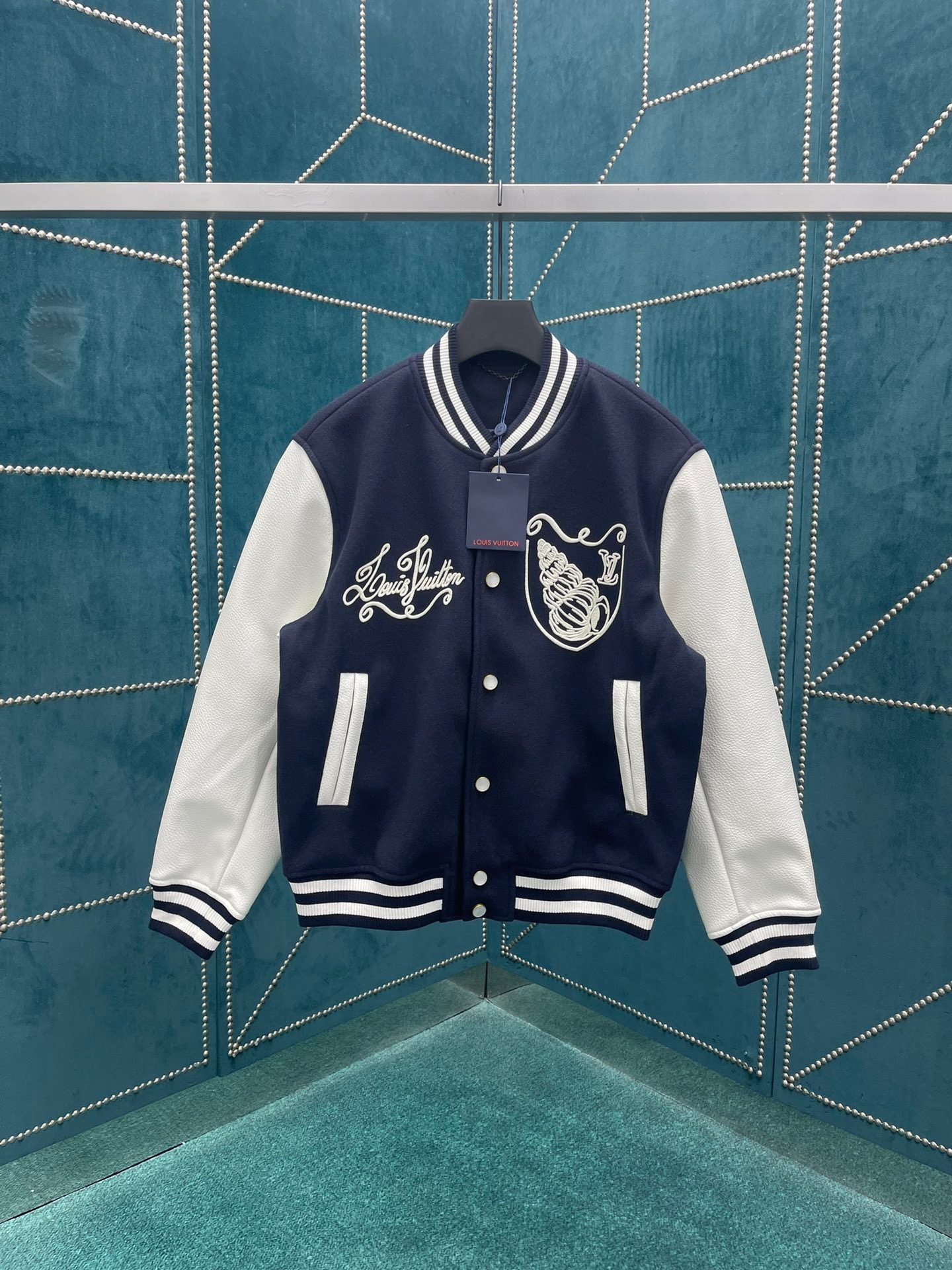 The new 24ss baseball jacket from Lvjia combines a sheep sweater body and leather sleeves, injecting a nautical vibe into the classic silhouette. The LV Seashells embroidery on the garment features a vintage Louis Vuitton logo and exquisite shell patterns, with the LV letters on the back resembling a sailor knot and pearl buttons adding a touch of sophistication. Same gender design!